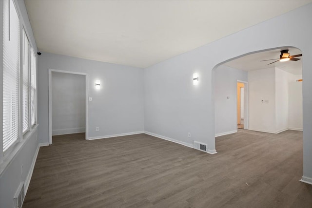 empty room with arched walkways, visible vents, and dark wood finished floors