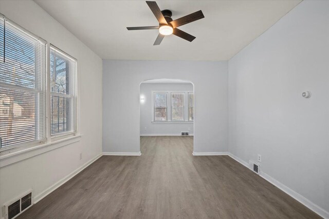 spare room featuring arched walkways, visible vents, baseboards, and wood finished floors