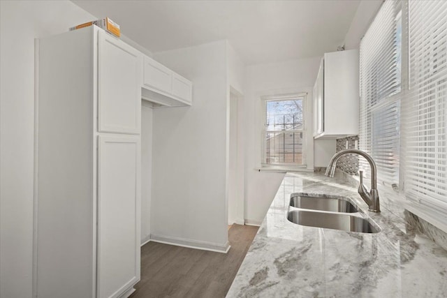 kitchen featuring a sink, baseboards, white cabinets, light stone countertops, and dark wood finished floors