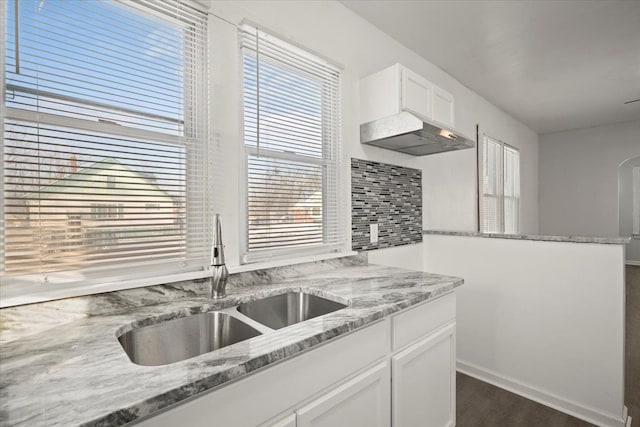 kitchen featuring light stone countertops, a sink, white cabinetry, decorative backsplash, and dark wood-style floors