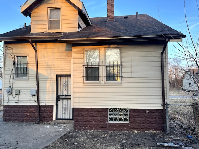 back of house featuring a chimney, roof with shingles, and fence