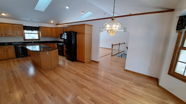 kitchen with a sink, black appliances, lofted ceiling with skylight, dark countertops, and pendant lighting