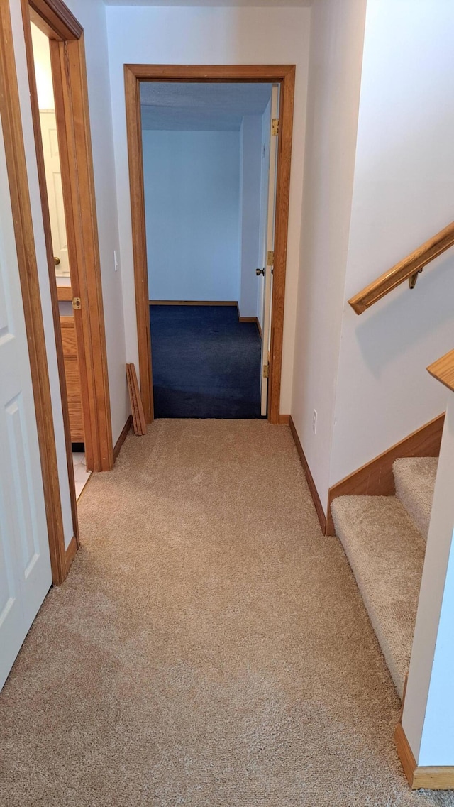 corridor with light colored carpet, stairway, and baseboards