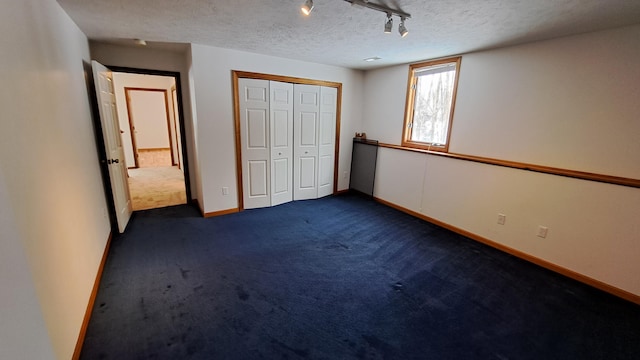 unfurnished bedroom with rail lighting, baseboards, dark carpet, and a textured ceiling