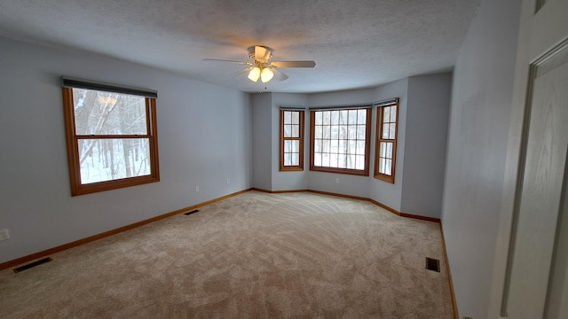 spare room with light carpet, a textured ceiling, visible vents, and baseboards