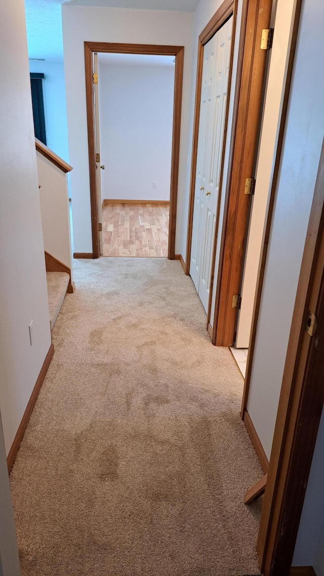 corridor with light carpet, stairs, and baseboards