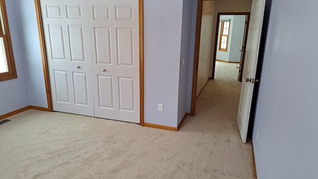 unfurnished bedroom featuring baseboards, a closet, and light colored carpet