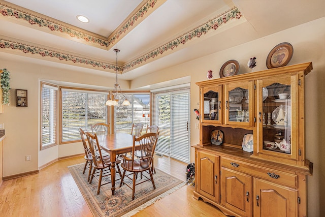 dining room featuring light wood-style floors, baseboards, and a tray ceiling