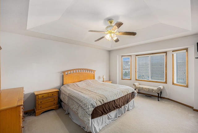 bedroom with a ceiling fan, a raised ceiling, light colored carpet, and baseboards