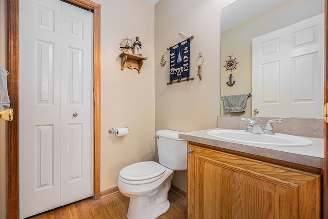 half bathroom featuring a closet, toilet, vanity, wood finished floors, and baseboards