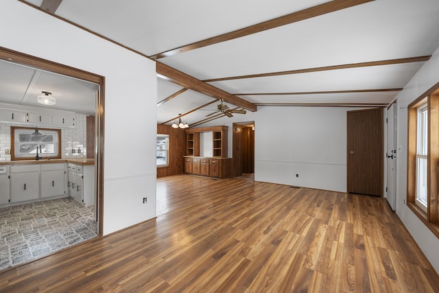 unfurnished living room with light wood-type flooring, an inviting chandelier, lofted ceiling with beams, and a sink