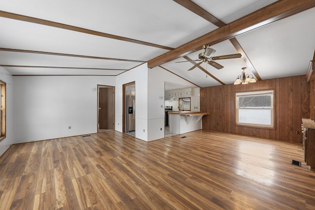 unfurnished living room with lofted ceiling with beams, wood walls, ceiling fan with notable chandelier, and wood finished floors