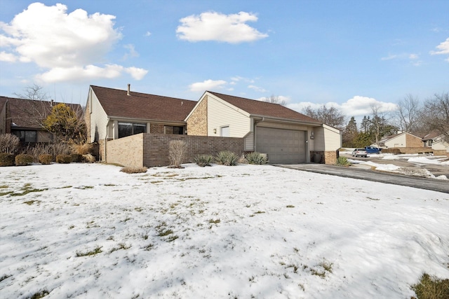 view of snowy exterior featuring a garage, brick siding, and fence