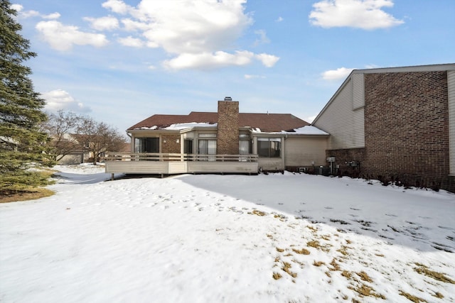 snow covered back of property with a chimney, brick siding, and a deck