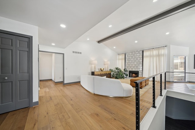 living area featuring a fireplace, vaulted ceiling with beams, visible vents, light wood-type flooring, and baseboards