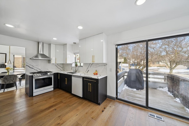 kitchen with a sink, white cabinetry, wall chimney range hood, stainless steel range with gas cooktop, and dishwasher