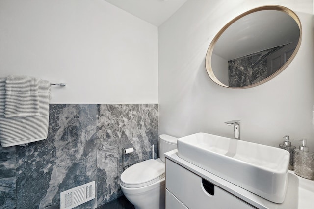 bathroom featuring toilet, visible vents, tile walls, and vanity