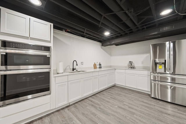 kitchen featuring light countertops, appliances with stainless steel finishes, white cabinets, a sink, and light wood-type flooring