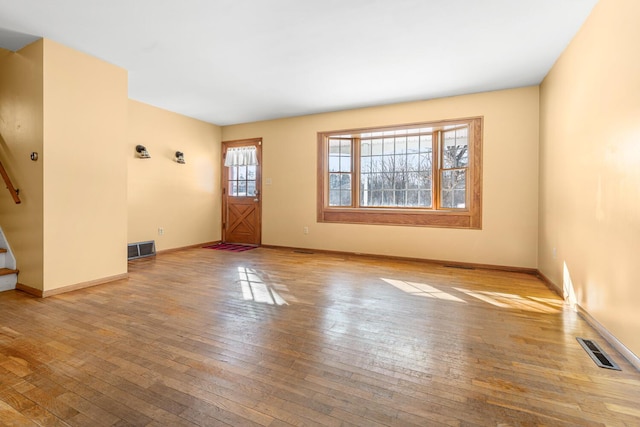 unfurnished living room featuring light wood-type flooring, visible vents, baseboards, and stairs