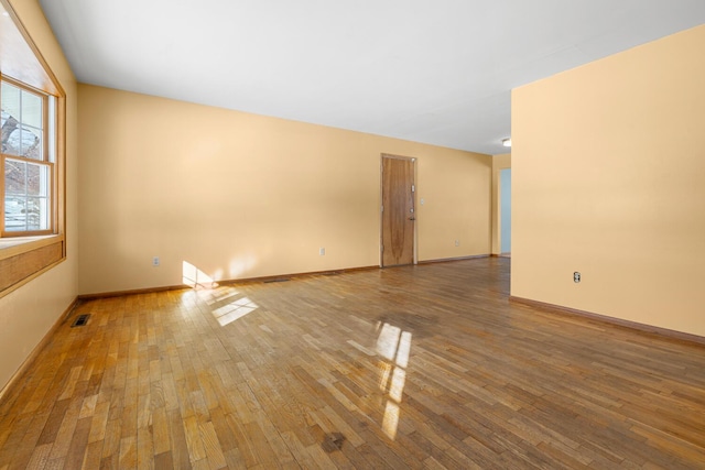 empty room featuring wood finished floors, visible vents, and baseboards