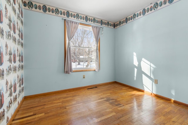 spare room featuring baseboards, visible vents, and wood finished floors