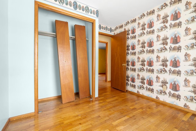 unfurnished bedroom with wallpapered walls, light wood-style flooring, and baseboards