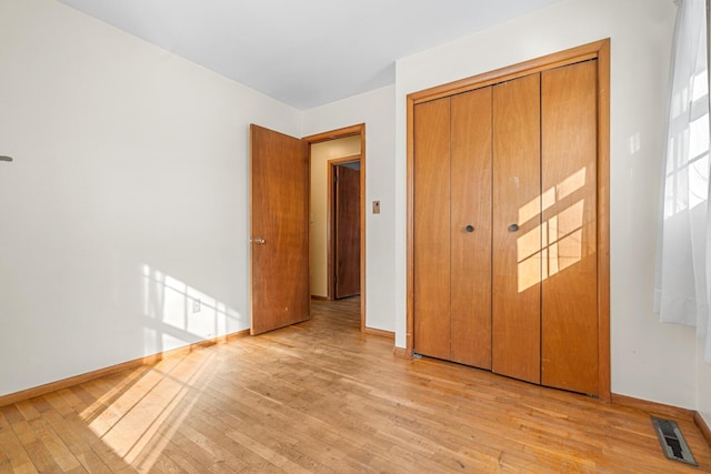 unfurnished bedroom with light wood-type flooring, a closet, visible vents, and baseboards