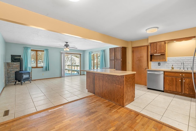 kitchen with brown cabinets, light countertops, stainless steel dishwasher, open floor plan, and a sink