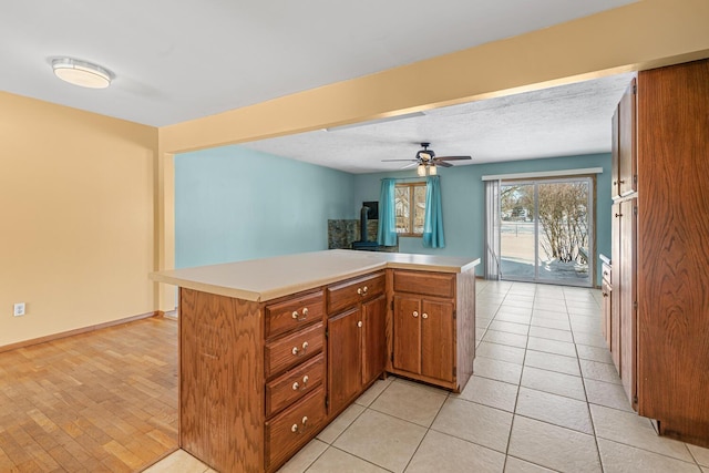 kitchen with light countertops, brown cabinetry, a ceiling fan, a textured ceiling, and a peninsula