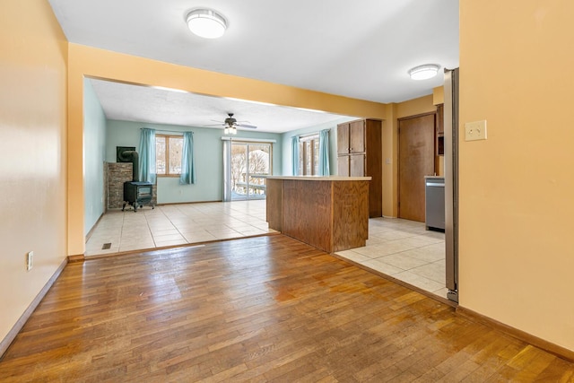 kitchen with a peninsula, light wood-style floors, open floor plan, brown cabinetry, and a wood stove