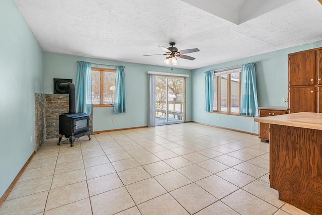 living room with light tile patterned floors, ceiling fan, a textured ceiling, and a wood stove