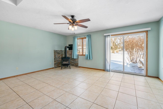 spare room featuring a textured ceiling, light tile patterned floors, a ceiling fan, baseboards, and a wood stove