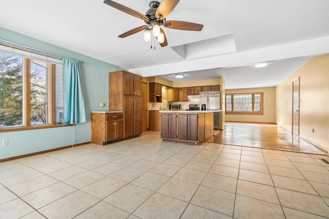 kitchen featuring light tile patterned floors, brown cabinetry, open floor plan, stainless steel appliances, and light countertops