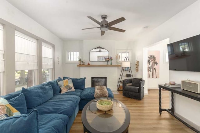 living area featuring light wood finished floors, a fireplace, a ceiling fan, and baseboards