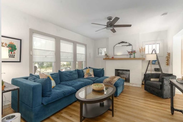 living area featuring a ceiling fan, a fireplace, and wood finished floors