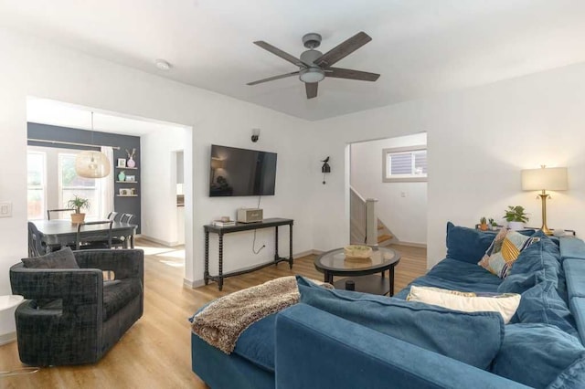 living room featuring light wood-type flooring, stairs, baseboards, and a ceiling fan