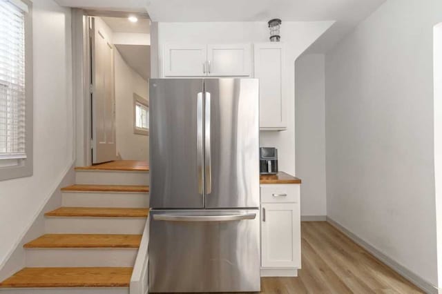 kitchen featuring light wood finished floors, freestanding refrigerator, white cabinetry, butcher block countertops, and baseboards