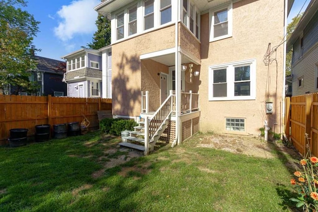 rear view of house with a fenced backyard, a lawn, and stucco siding