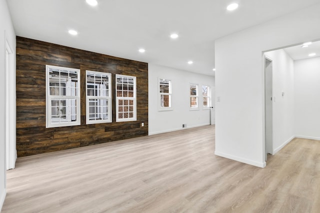 unfurnished living room featuring light wood-type flooring, wooden walls, and recessed lighting