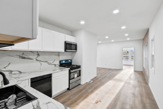 kitchen featuring stainless steel appliances, decorative backsplash, white cabinets, light stone countertops, and light wood-type flooring