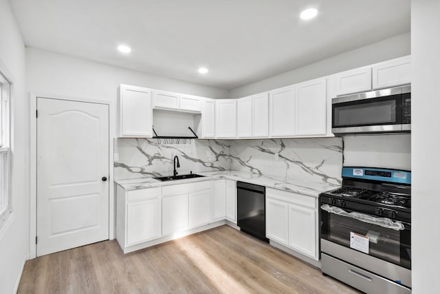 kitchen with stainless steel appliances, white cabinets, a sink, and light stone countertops