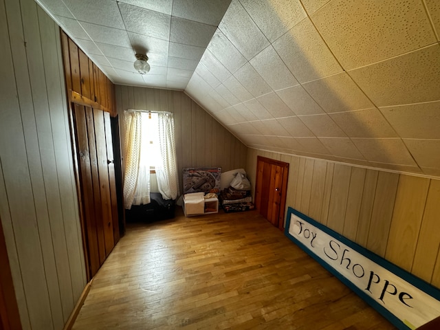 bonus room featuring light wood-style floors, vaulted ceiling, and wood walls