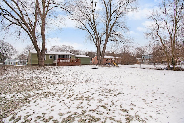 snowy yard featuring a playground and a wooden deck