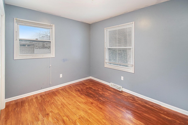 empty room featuring wood finished floors, visible vents, and baseboards