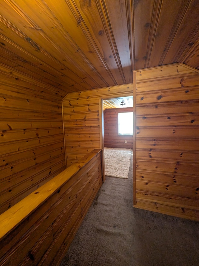 hallway with dark colored carpet, wood ceiling, wood walls, and lofted ceiling