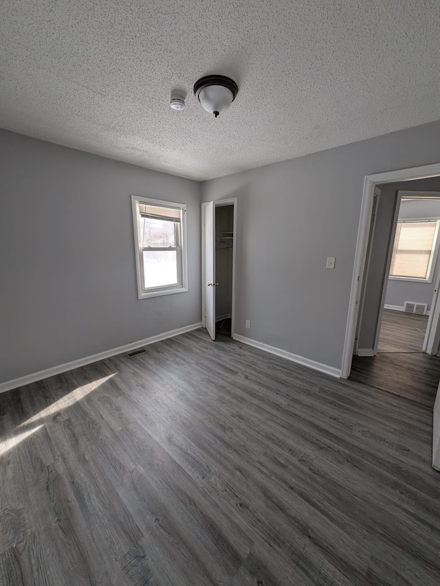 unfurnished bedroom with visible vents, dark wood finished floors, a textured ceiling, and baseboards