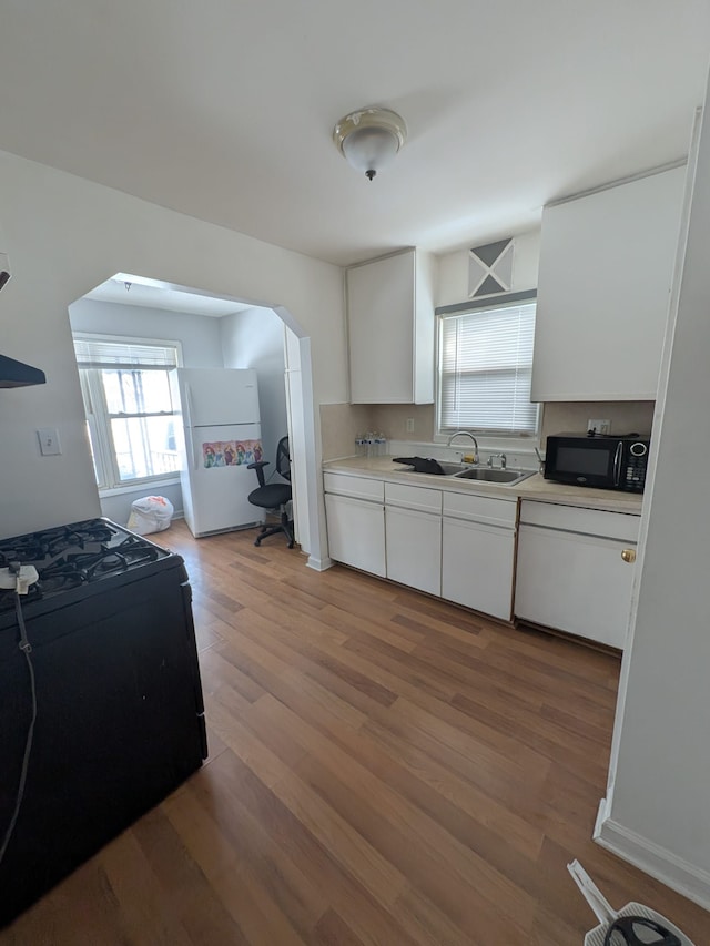 kitchen featuring black microwave, light countertops, freestanding refrigerator, and white cabinetry