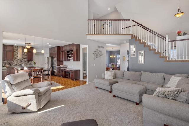 living area with a chandelier, high vaulted ceiling, visible vents, stairway, and light wood-type flooring