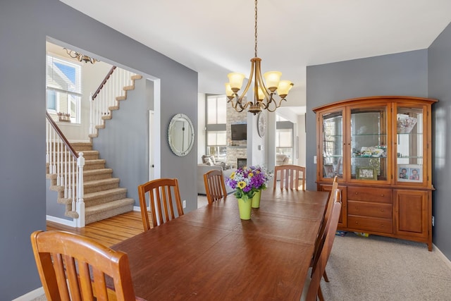 dining room featuring a chandelier, a fireplace, baseboards, and stairs