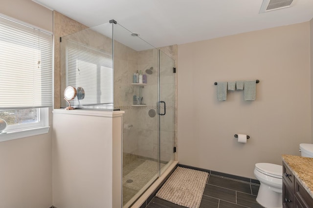 bathroom with visible vents, toilet, vanity, a shower stall, and baseboards